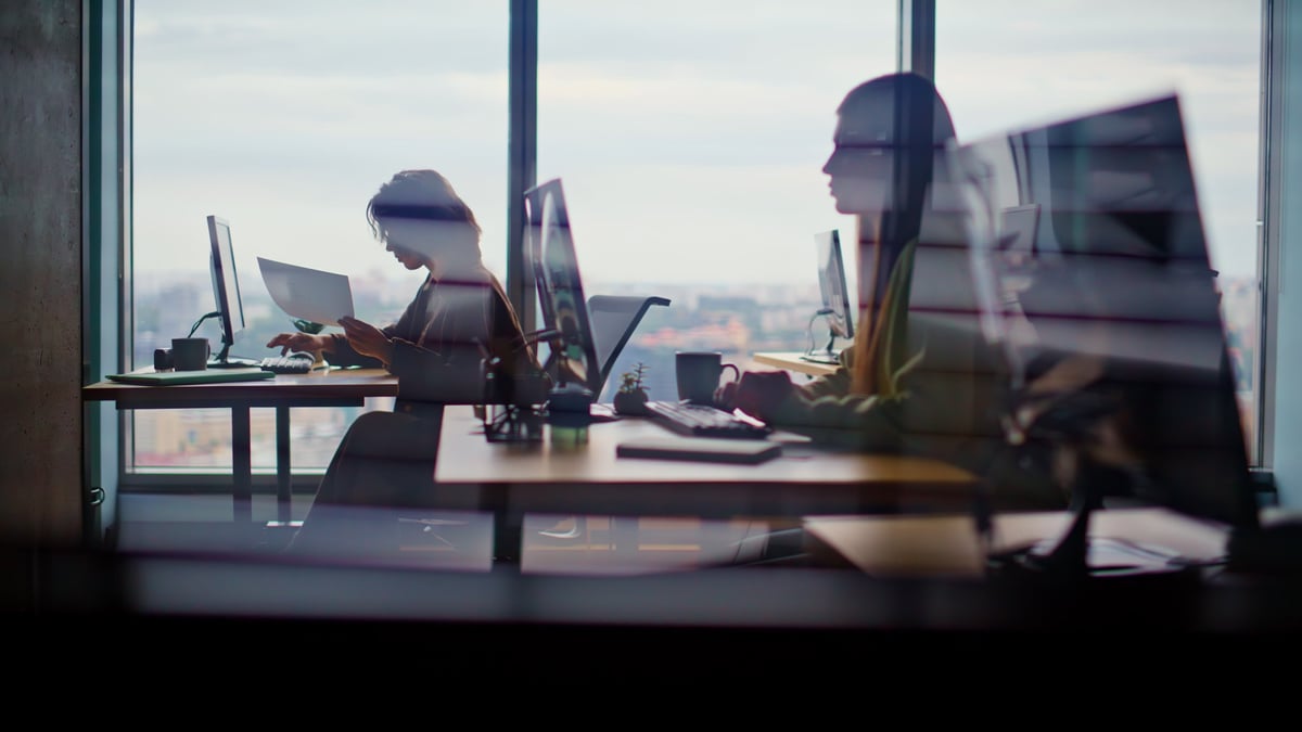 Busy corporate office with people working at computers against a cityscape window