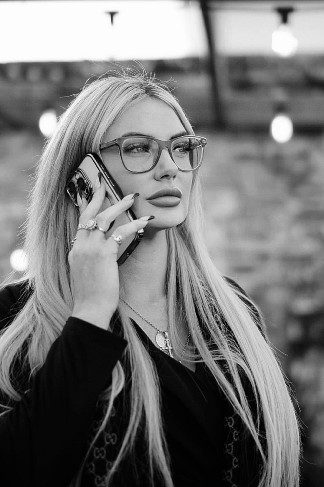 Woman with long blonde hair and glasses talking on a smartphone in black and white portrait photography